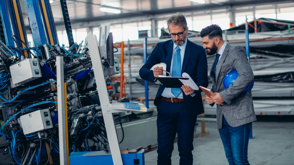 Two men in suits discussing plans in a manufacturing factory